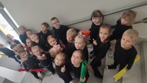Dzieci w czarnych strojach stoją na schodach. W rękach trzymają flagi w kolorach tęczy.