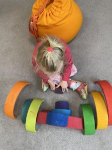 Dziecko siedzi i kukłada z kloców kolorową tęczę.