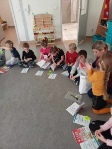 Dzieci siedzą w kole na dywanie, przed sobą mają kolorowanki i gadżety, które przyniosła pani Sylwia, mama Tymka Idziorka.