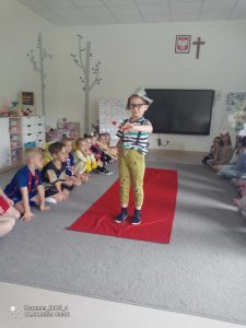 Na czerwonym dywanie stoi chłopiec przebrany w strój malarza.