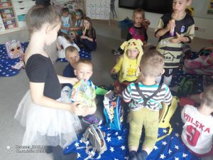 Dzieci siedzą na piknikowych kocach i częstują się smakołykami z przyniesionych plecaków.