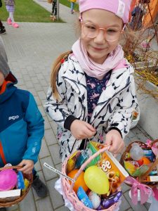Dzieci trzymają koszyczki wielkanocne w rękach, stoją przed budynkiem przedszkola i uśmiechają się. W koszyczkach są słodycze.