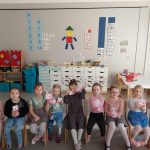 Dziewczynki siedzą na krzesełkach i uśmiechają się, pokazują prezenty otrzymane od chłopców.