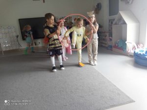 Dziewczynka przechodzi przez obręcz trzymaną przez chłopców.