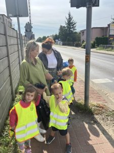 Dzieci wraz z opiekunami stoją przed przejściem dla pieszych i czekają na zielone światło.