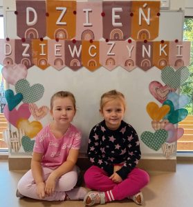 Dwie dziewczynki siedza przy fotobudce serduszkami i z napisem dzień dziewczynki.