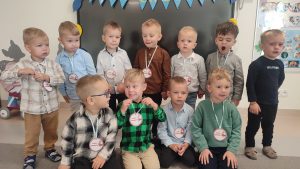 Grupa chłopców ubrani odświętnie pozuje do wspólnego zdjęcia z prezentami, medalami i balonami.
