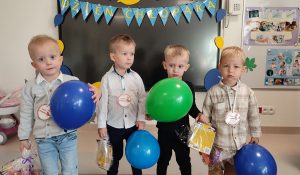 Grupa chłopców ubrani odświętnie pozuje do wspólnego zdjęcia z prezentami, medalami i balonami.