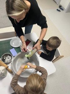 Dzieci z nauczycielem wsypują kolekne składniki do miski aby stworzyć masę porcelanową.