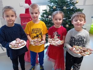 dwie dziewczynki i dwóch chłopców stoi przy choince. W rękach trzymają talerz z piernikami