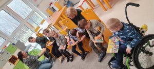 Dzieci siedzą na krzesełkach i oglądają książeczki.