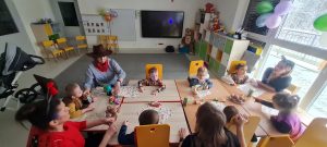 Dzieci siedzą przy stolikach i częstują się przekąskami podczas baliku karnawałowego.
