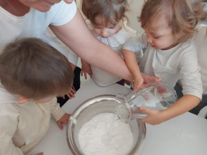 Dzieci wlewają wodę do miski z mąką aby stworzyć białą masę.