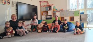 Dzieci siedzą na dywanie i trzymają w rękach swoje misie.