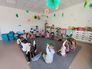 Przedszkolaki siedzą na dywanie w kole trzymając w ręce zielone kartki - tym sposobem odpowiadają na zadane przez nauczycielkę pytanie.