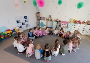 Grupa dzieci siedzi w kole na dywanie - podają sobie motek wełny tworząc sieć komputerową.