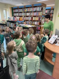 Dzieci słuchają pani bibliotekarki i poznają zasady korzystania z biblioteki.