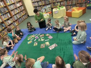 Dzieci siedzą na dywanie i odpowiadają na pytania zadawane przez panią bibliotekarkę dotyczące wiosny.