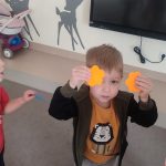 Dzieci trzymają do góry ręce, w których trzymają dwa kolorowe kwiatki.