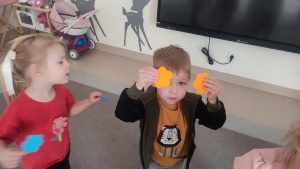 Dzieci trzymają do góry ręce, w których trzymają dwa kolorowe kwiatki.