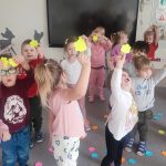 Dzieci trzymają do góry ręce, w których trzymają jeden żółty kwiatek.