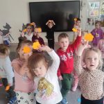 Dzieci trzymają do góry ręce, w których trzymają jeden pomarańczowy kwiatek.