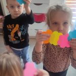 Dzieci trzymają do góry ręce, w których trzymają dwa kolorowe kwiatki.