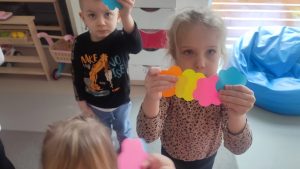 Dzieci trzymają do góry ręce, w których trzymają dwa kolorowe kwiatki.