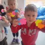 Dzieci trzymają do góry ręce, w których trzymają dwa kolorowe kwiatki.