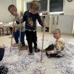 Dwóch chłopców ma założone na nogach "narty" i wjeżdżają w górkę śniegu.