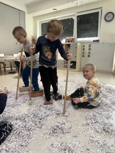 Dwóch chłopców ma założone na nogach "narty" i wjeżdżają w górkę śniegu.