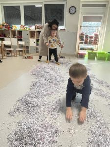 Dziecko z pomocą nauczyciela sunie po papierowym śniegu.