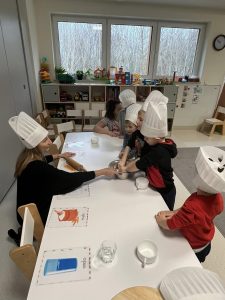 Dzieci zagniatają swoimi rączkami ciasto na pizzę.