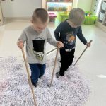 Dwóch chłopców ma założone na nogach "narty" i wjeżdżają w górkę śniegu.