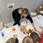 Nauczyciel pokazuje dzieciom z jakich produktów powstaje pizza.