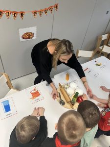 Nauczyciel pokazuje dzieciom z jakich produktów powstaje pizza.