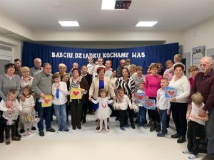 Dzieci z Babciami i Dziedkami stoją na środku sali i pozują do zdjęcia.