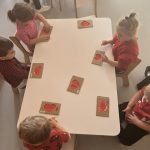 Dzieci siedzą przy stoliczkach i tworzą pracę plastyczną- czerwone seruszka z farby.
