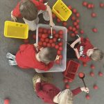 Dzieci wyciągają z dużego białego pojemnika za pomocą łyżek cedzakowych czerwone piłeczki.