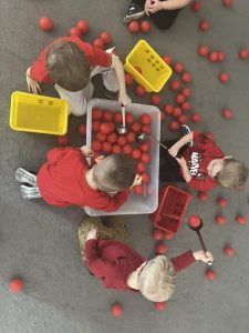 Dzieci wyciągają z dużego białego pojemnika za pomocą łyżek cedzakowych czerwone piłeczki.