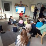 Dzieci siedzą na dywanie i słuchają opowiadania.