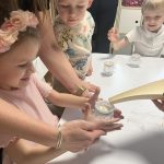 Dzieci z pomocą nauczyciela i opiekuna wlewają wodę do słoiczka z gazą.