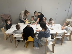 Dzieci z pomocą nauczyciela i opiekuna wlewają wodę do słoiczka z gazą.