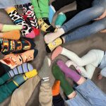 Dzieci siedzą w kole i pokazują eksponują swoje kolorowe skarpetki, które są symbolem solidarności z osobami z Zespołem Downa.