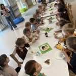 Dzieci siedzą przy stoliczku i degustują samodzielnie udekorowane gofry.