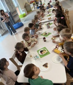 Dzieci siedzą przy stoliczku i degustują samodzielnie udekorowane gofry.