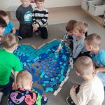 Chłopcy układają z niebieskich klocków duże serduszko na szarym dywanie.