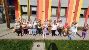 Duża grupa dzieci pozuje do zdjęcia na tle budynku w kolorowe paski. Dzieci w rękach trzymają wielkanocne koszyczki.