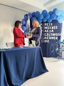 Pani Dyrektor stojąca naprzeciwko Pani prowadzącej warsztaty wręczająca kwiat.