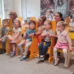 Dzieci siedzą na krzesełkach i słuchają koncertu muzycznego